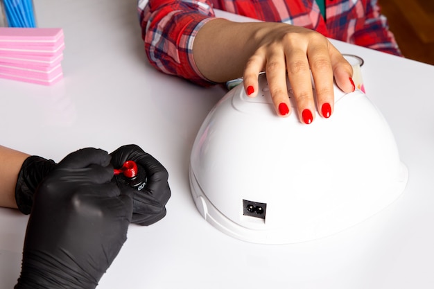 Una vista frontal mujer joven manicura con guantes negros haciendo manicura en blanco