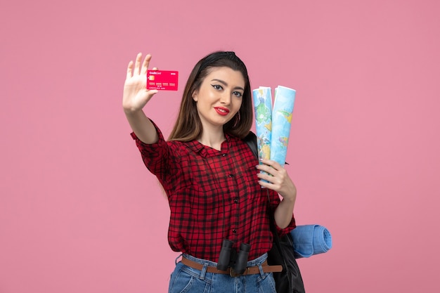 Vista frontal mujer joven con mapas y tarjeta bancaria en el color humano de la mujer de fondo rosa