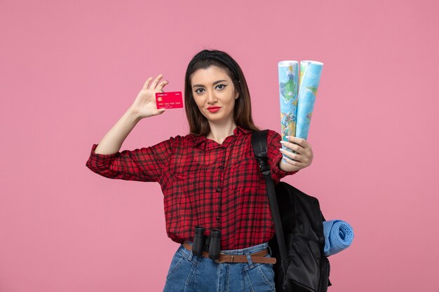 Vista frontal mujer joven con mapas y tarjeta bancaria en el color humano de la mujer de fondo rosa