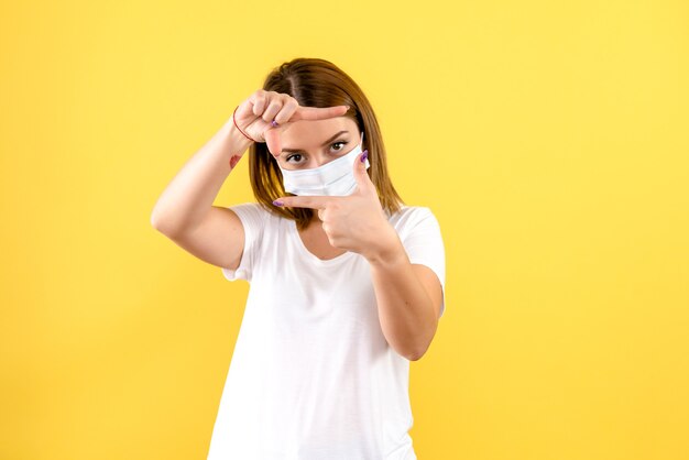 Vista frontal de la mujer joven en máscara estéril en pared amarilla