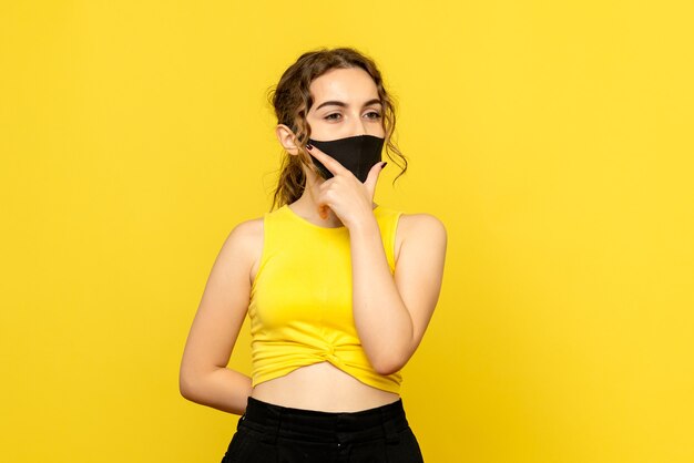 Vista frontal de la mujer joven en máscara negra sobre piso amarillo virus de emoción covid