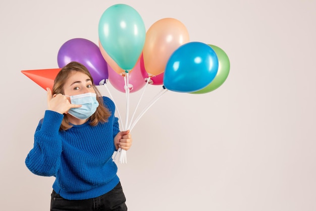 Foto gratuita vista frontal mujer joven en máscara sosteniendo globos de colores