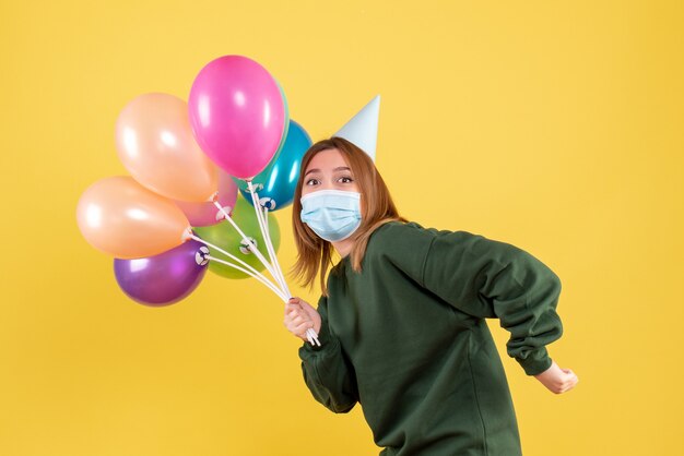 Vista frontal mujer joven en máscara sosteniendo globos de colores