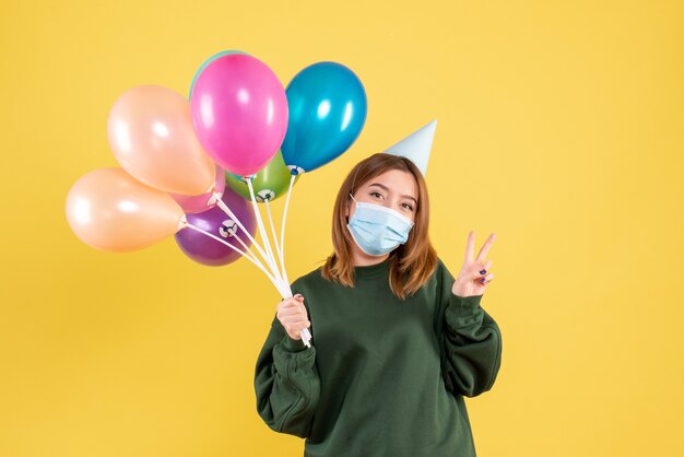 Vista frontal mujer joven en máscara sosteniendo globos de colores