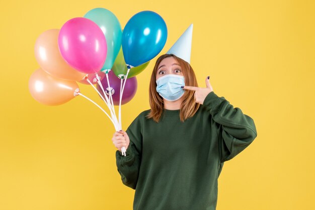 Vista frontal mujer joven en máscara sosteniendo globos de colores