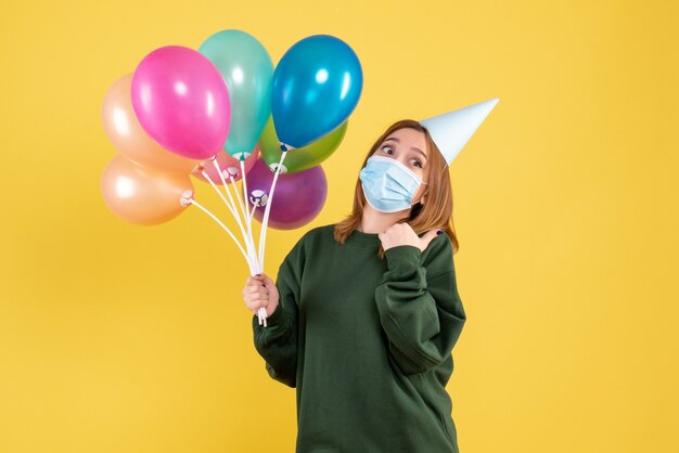 Vista frontal mujer joven en máscara sosteniendo globos de colores