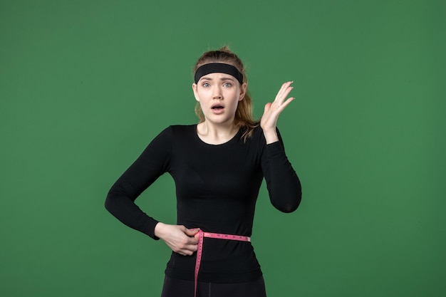 Vista frontal de la mujer joven midiendo su cuerpo con centímetro sobre fondo verde mujer deporte color salud cuerpo atleta entrenamiento en forma