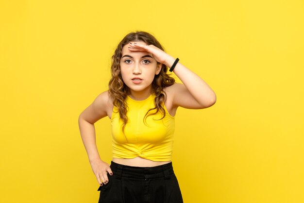 Vista frontal de la mujer joven mirando a distancia en la pared amarilla