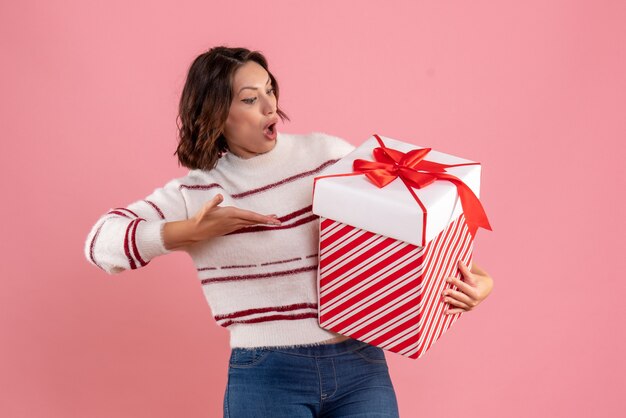 Vista frontal de la mujer joven con Navidad presente en la pared rosa