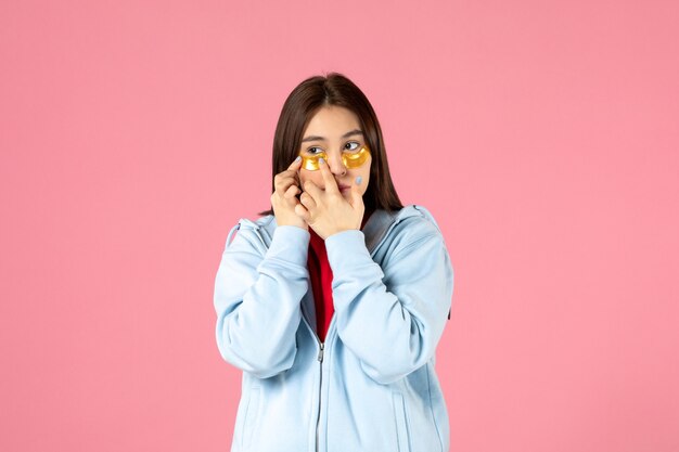 Vista frontal de la mujer joven con parches en los ojos debajo de los ojos en la pared rosa