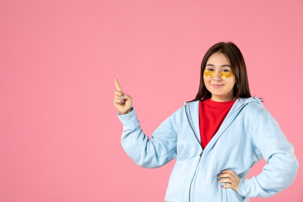 Vista frontal de la mujer joven con parches en los ojos debajo de los ojos en la pared rosa