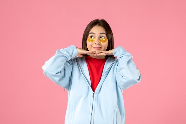 Vista frontal de la mujer joven con parches en los ojos debajo de los ojos en la pared rosa