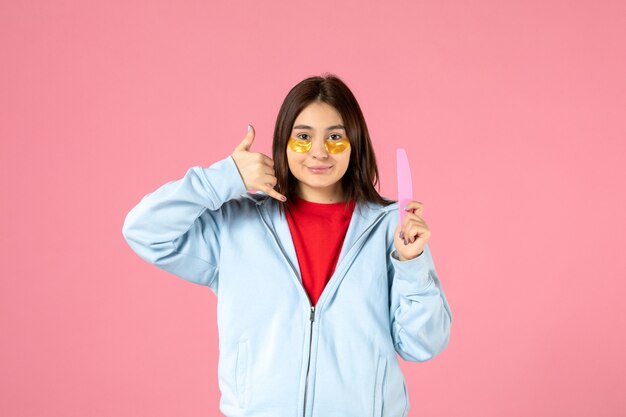 Vista frontal de la mujer joven con parches en los ojos y lima de uñas en la pared rosa