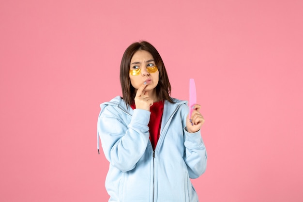 Vista frontal de la mujer joven con parches en los ojos y lima de uñas en la pared rosa