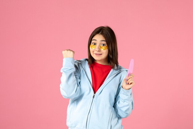 Vista frontal de la mujer joven con parches en los ojos y lima de uñas en la pared rosa