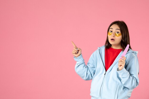 Vista frontal de la mujer joven con parches en los ojos y lima de uñas en la pared rosa