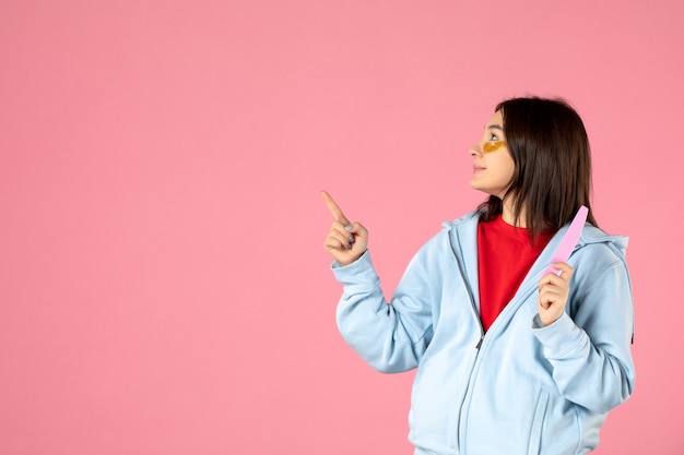 Vista frontal de la mujer joven con parches en los ojos y lima de uñas en la pared rosa