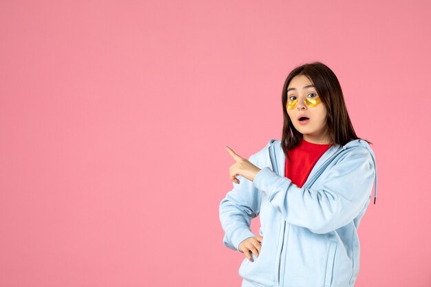 Vista frontal de la mujer joven con parches en los ojos en la pared rosa