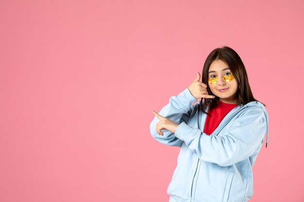 Vista frontal de la mujer joven con parches en los ojos en la pared rosa