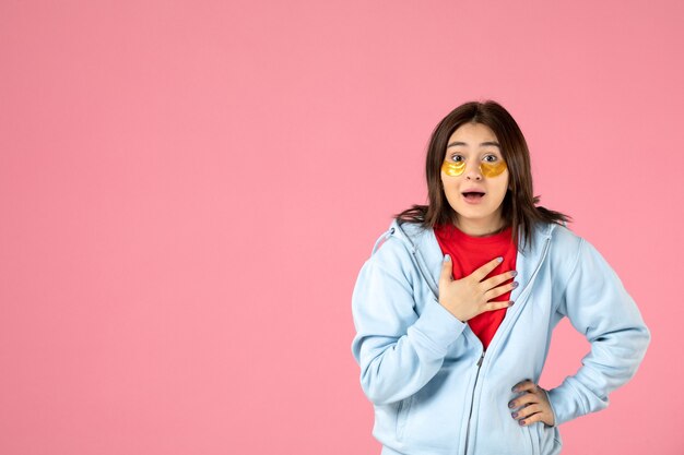 Vista frontal de la mujer joven con parches en los ojos en la pared rosa