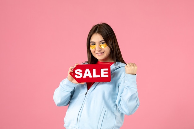 Foto gratuita vista frontal de la mujer joven con parches en los ojos sosteniendo pancartas de venta en la pared rosa