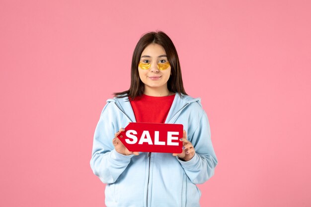 Vista frontal de la mujer joven con parches en los ojos sosteniendo pancartas de venta en la pared rosa