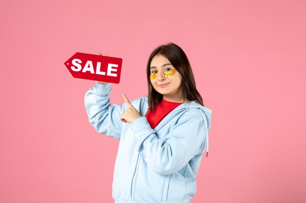 Vista frontal de la mujer joven con parches en los ojos sosteniendo pancartas de venta en la pared rosa