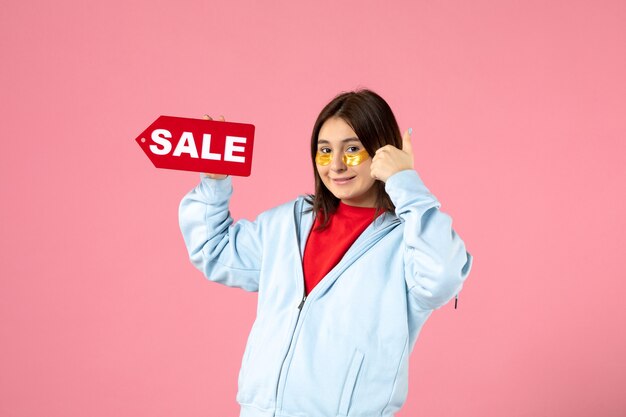 Vista frontal de la mujer joven con parches en los ojos sosteniendo pancartas de venta y sonriendo en la pared rosa