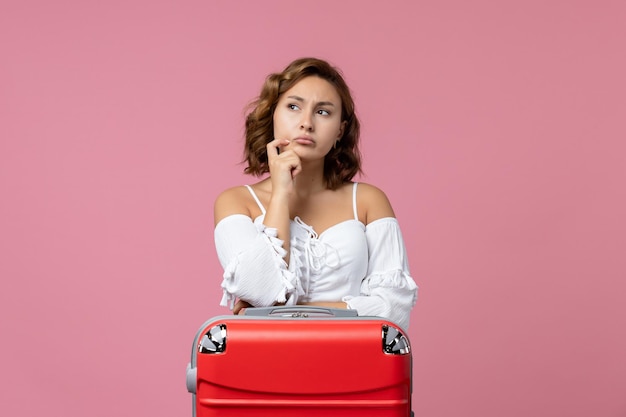 Vista frontal de la mujer joven pensando con bolsa de vacaciones roja en la pared rosa