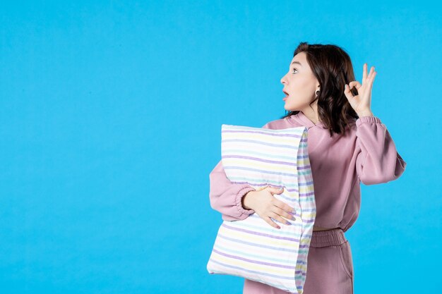 Vista frontal mujer joven en pijama rosa con almohada en azul