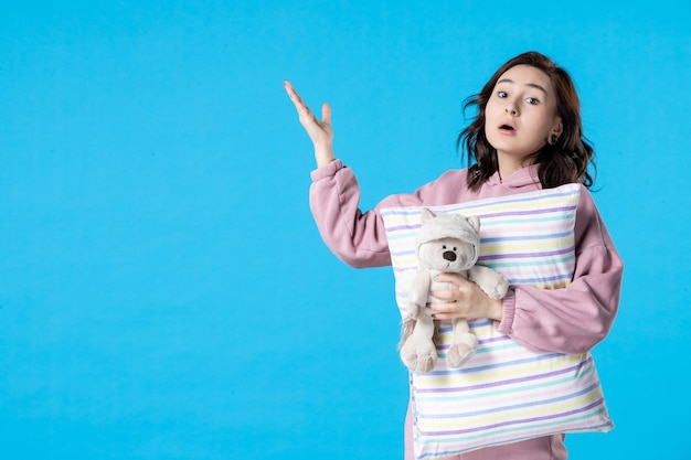 Vista frontal mujer joven en pijama rosa con osito de juguete y almohada en mujer azul
