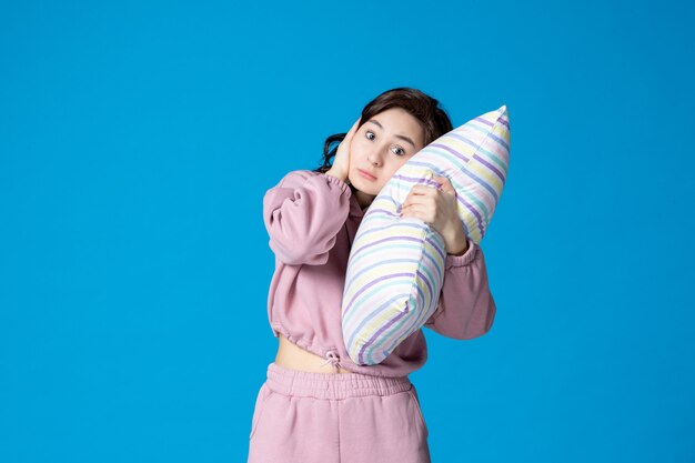 Vista frontal mujer joven en pijama rosa sosteniendo la almohada en la pared azul noche color fiesta insomnio reposo en cama sueño mujer sueño