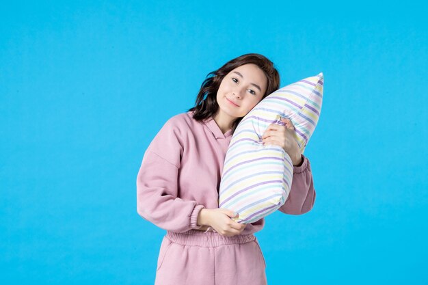 Vista frontal mujer joven en pijama rosa sosteniendo la almohada en la pared azul noche color insomnio reposo en cama sueño mujer beso fiesta emoción dormir