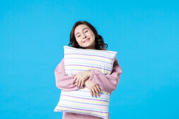 Vista frontal mujer joven en pijama rosa sosteniendo la almohada en la pared azul noche color reposo en cama emoción modelo sueño mujer sueño