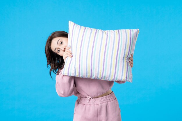 Vista frontal mujer joven en pijama rosa sosteniendo la almohada en la pared azul noche color reposo en cama emoción mujer sueño insomnio