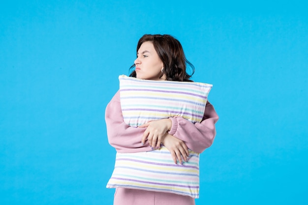 Vista frontal mujer joven en pijama rosa sosteniendo la almohada en la pared azul noche color reposo en cama sueño emoción modelo sueños mujer