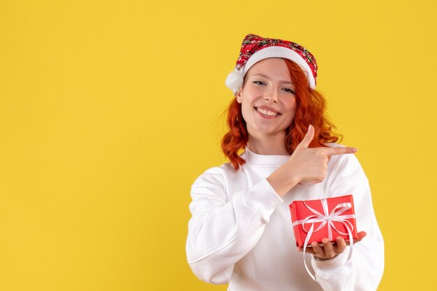 Vista frontal de la mujer joven con poco presente de Navidad en la pared amarilla