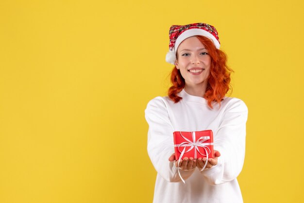 Vista frontal de la mujer joven con poco presente de Navidad en la pared amarilla