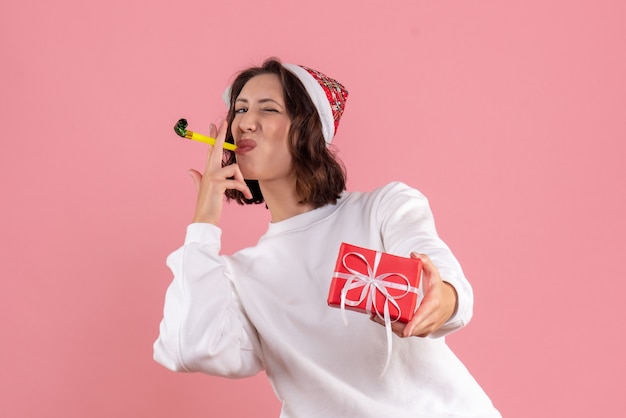 Vista frontal de la mujer joven con poco presente de Navidad en la pared rosa