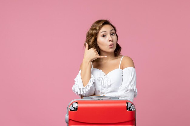 Vista frontal de la mujer joven posando con bolsa de vacaciones roja en la pared de color rosa claro