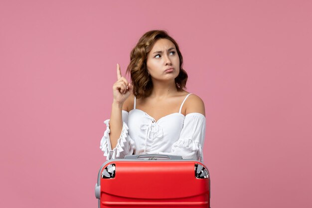 Vista frontal de la mujer joven posando con bolsa de vacaciones roja en la pared rosa