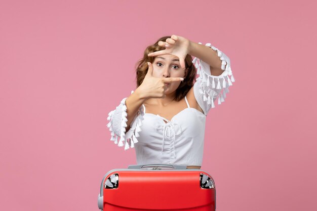 Vista frontal de la mujer joven posando con bolsa de vacaciones roja en la pared rosa