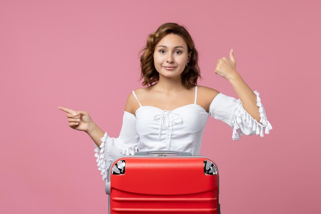 Vista frontal de la mujer joven posando con bolsa de vacaciones roja en la pared rosa