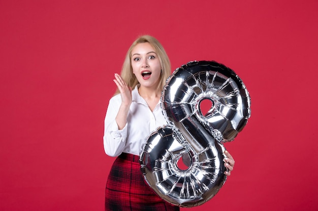 Vista frontal mujer joven posando con globo plateado como símbolo de marcha sobre fondo rojo igualdad feminidad femenina día de la mujer color sensual