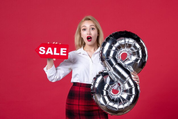 Vista frontal mujer joven posando con globo plateado y placa de identificación de venta sobre fondo rojo femenino horizontal igualdad sensual día de la mujer feminidad cariñosa