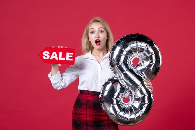 Vista frontal mujer joven posando con globo plateado y placa de identificación de venta sobre fondo rojo femenino horizontal igualdad sensual día de la mujer feminidad cariñosa