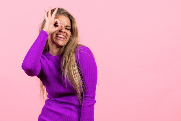 Vista frontal de la mujer joven posando en un hermoso vestido morado en la pared rosa