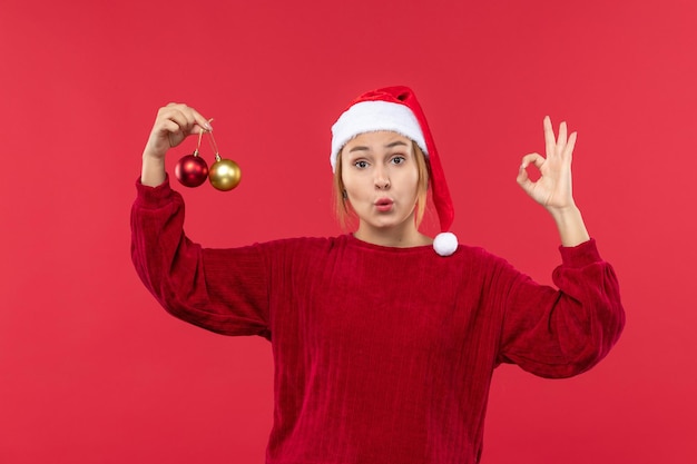 Vista frontal mujer joven posando con juguetes de navidad en la emoción de navidad de vacaciones de escritorio rojo