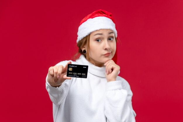 Vista frontal mujer joven posando con tarjeta bancaria en el escritorio rojo