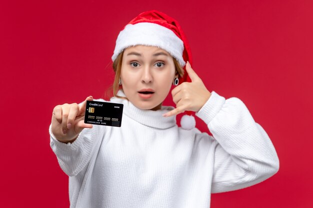 Vista frontal mujer joven posando con tarjeta bancaria en el fondo rojo.